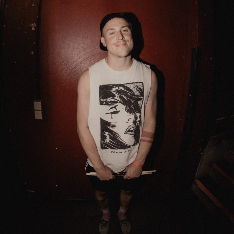 A member of Melonball smiling in the camera holding drum sticks.